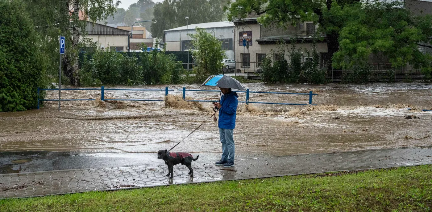 Muž s deštníkem a psem stojí na zatopené ulici při povodni